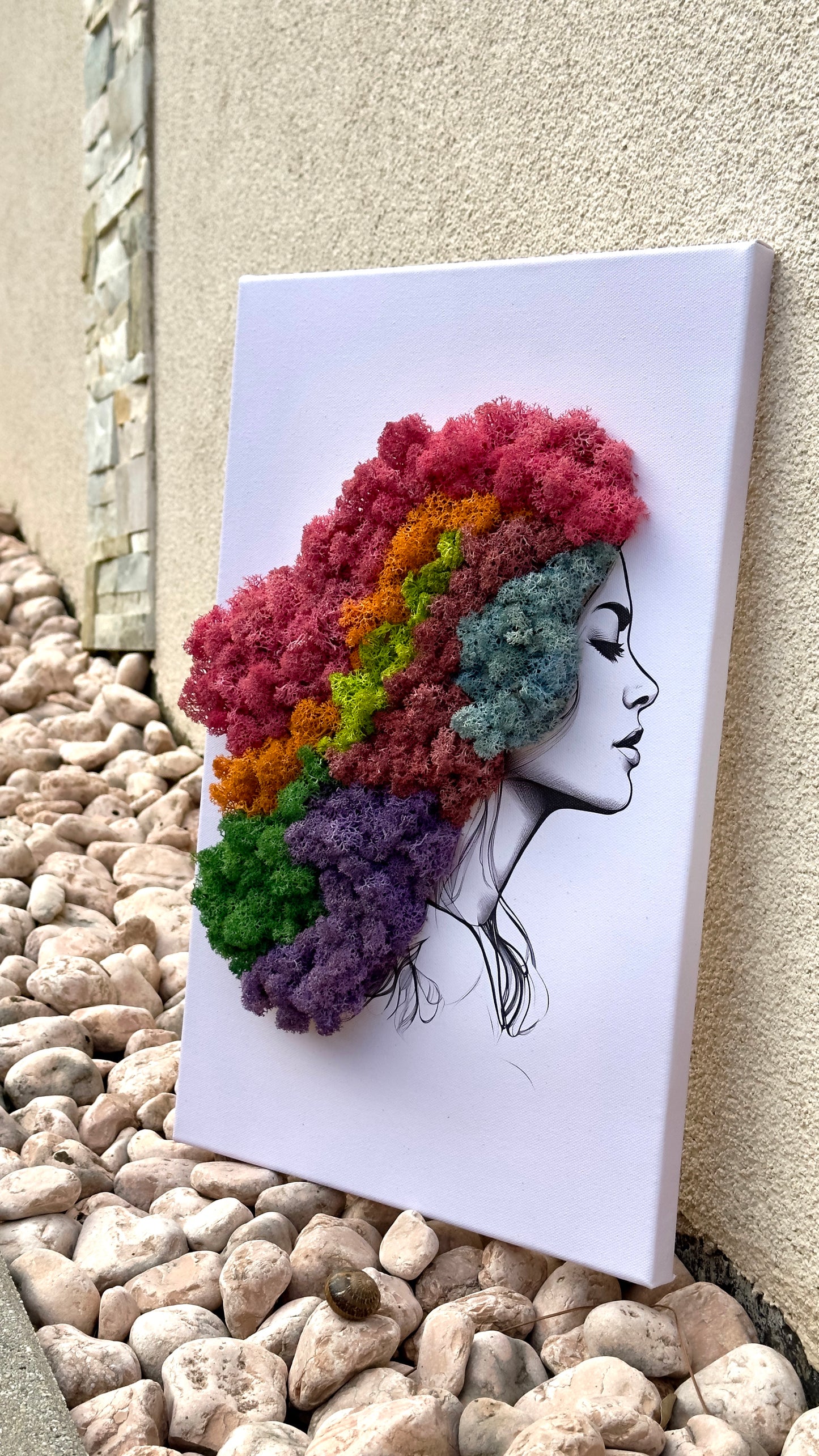 Canvas art of a woman with colorful preserved moss hair on a pebble surface.